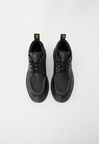 Zapatos de cuero negros con punta redonda, costuras amarillas y una lengüeta en el talón. Presentan un diseño clásico de cordones y una parte superior texturizada.