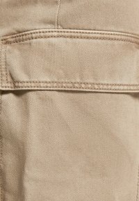 Tela color marrón claro con una sutil textura y un detalle de bolsillo cosido. El material es suave, duradero y está diseñado para un uso casual.