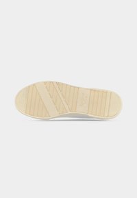 Semelle unique de chaussure de sport beige avec motifs d'adhérence texturés et nom de la marque embossé sur le talon, vue de dessous sur fond blanc.