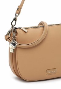 Beżowa torebka z fakturą sztucznej skóry, zapinana na zamek, z okrągłą rączką i srebrnymi okuciami. Ozdobiona brelokiem w kształcie serca.