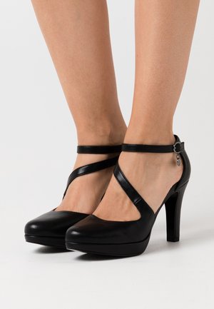 Black leather high-heel shoes with a platform, featuring a cross strap design and ankle buckle. Smooth texture and rounded toe shape.