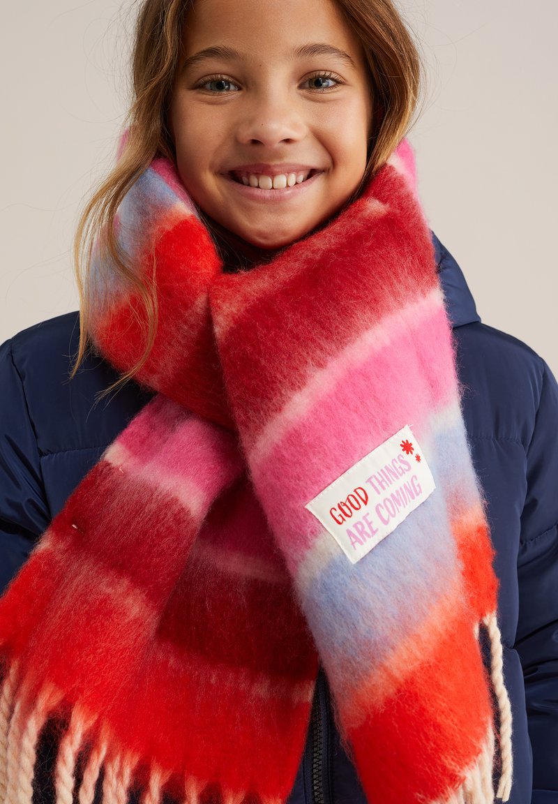 Farverig tørklæde med røde, pink og blå striber. Blød, fluffy tekstur med en lap, der siger "GODE TING KOMMER" i hvid og rød.