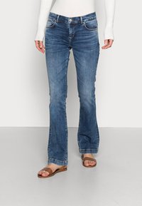 Blue flared jeans with a medium wash, featuring front pockets, a zipper fly, and subtle fading. Paired with brown flat sandals.