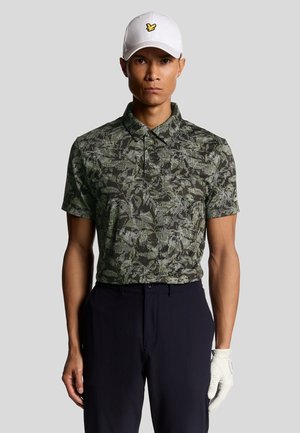 Uomo che indossa un cappello bianco con logo giallo, una polo a maniche corte verde scuro con motivo, pantaloni neri e un guanto da golf bianco sulla mano destra.