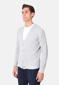 Cardigan grigio chiaro lavorato a maglia con scollo a V, sei bottoni, polsini e orlo a coste, realizzato in tessuto morbido, abbinato a pantaloni scuri.