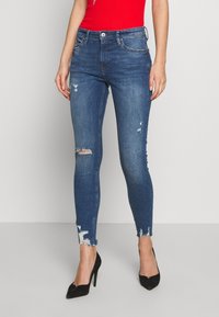 Jeans ajustados de color azul con detalles desgastados, que presentan roturas en las rodillas y dobladillos deshilachados. Fabricados en denim con una textura suave.