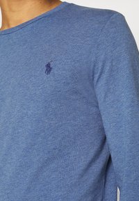 Herrskjorta med långa ärmar i heather blue tyg, med en ribbad rundhals och en liten broderad logotyp på bröstet.