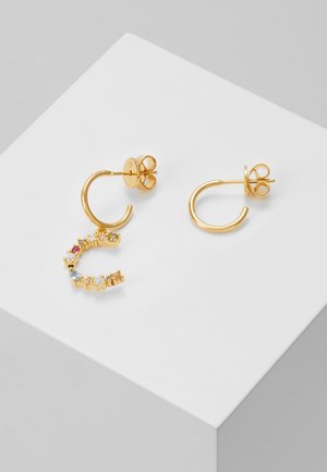 Paire de boucles d'oreilles créoles en or, dont l'une est ornée d'un pendentif semi-circulaire décoré de petites pierres précieuses multicolores, exposée sur une surface blanche.