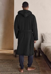Roba cu glugă neagră, cu o curea, realizată dintr-un material moale. Prezintă mâneci lungi și o croială lejeră, asortată cu pantaloni bleumarin și picioare goale.