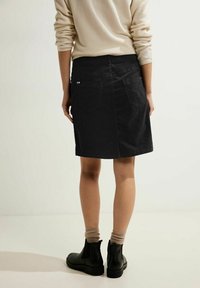 Sort denimnederdel med en tætsiddende talje, to baglommmer og lige snit. Båret med en beige sweater og sorte ankelstøvler.