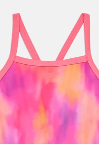 Τοπ μαγιό σε ροζ tie-dye με λεπτούς, σταυρωτούς ιμάντες. Το λείο ύφασμα έχει αποχρώσεις ροζ, πορτοκαλί και μωβ, με ένα μικρό λογότυπο.