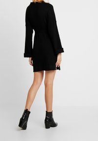 Svart ribbad klänning med långa ärmar och insvängd midja, med rak skärning och kortare avslut. Bärs med svarta ankelskor.