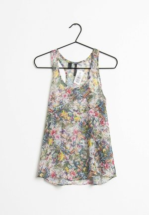 Kwiatowy bezrękawnik z wielokolorowymi kwiatami i zielenią na cienkiej tkaninie, wiszący na czarnym metalowym wieszaku na białym tle.