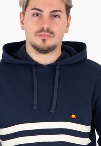 Felpa blu navy in cotone, con tasca a marsupio, cappuccio con coulisse e tre strisce bianche orizzontali accompagnate da un piccolo logo.