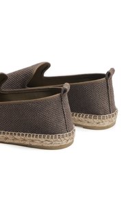 Chaussures slip-on en tissu marron avec un dessus texturé, doublure lisse contrastante et détail en corde de jute autour de la semelle. Onglets arrière pour un enfilage facile.