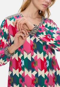 Mehrfarbige Bluse mit einem geometrischen Muster in Pink, Grün und Creme. Der Kragen und die Ärmelbündchen haben einen Akzent in Leopardenmuster.