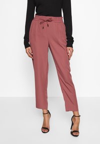 Losse roze broek met een elastische tailleband en trekkoorddetails, voorzien van zijzakken en een rechte pijpdesign. Draagt met zwarte hakken.