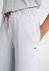 Graue Sweatpants mit einem elastischen Bund und Kordelzug, seitlichen Taschen und einem kleinen Logoaufnäher, gefertigt aus weichem Stoff mit glatter Textur.