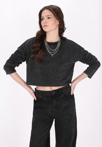 Felpa nera corta con maniche lunghe, texture morbida e aspetto sbiadito, abbinata a jeans neri a vita alta. Collana a catena in argento a strati.