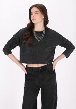 Schwarzer, verkürzter Sweatshirt mit langen Ärmeln, weicher Textur und verblasstem Aussehen, kombiniert mit hoch taillierten schwarzen Jeans. Silberne mehrlagige Kettenhalskette.