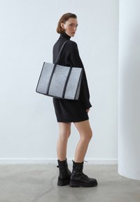 Szara torba na ramię z czarnymi skórzanymi akcentami, prostokątna forma, z dwoma solidnymi uchwytami i widocznymi detalami szycia.