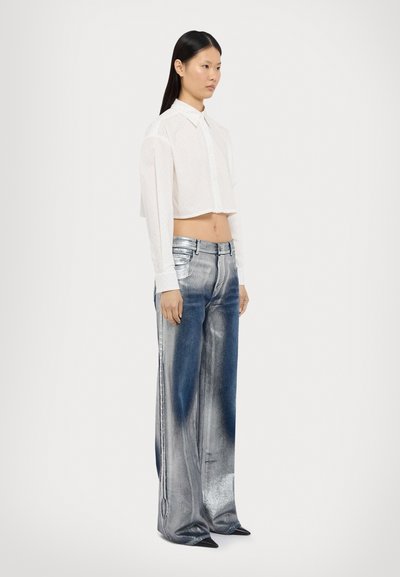 Camisa blanca con botones, recortada y con sutiles lunares, combinada con pantalones de pierna ancha brillantes en azul y plata, y zapatos negros de punta.