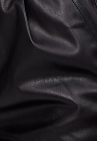 Svart strukturerad konstläder med synliga veck och sömnadsdetaljer på den övre högra sidan.