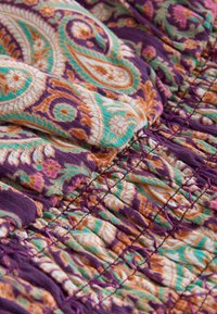 Lilla kangas oranži ja rohelise paisley mustriga. Kogutud tekstuur, millel on nähtavad õmblused, mis lisavad detaili ja mõõtmeid.