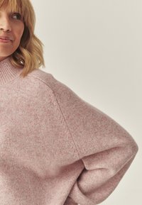 Różowy sweter z dzianiny o fakturowanej tkaninie, z wysokim kołnierzem i obniżonymi ramionami. Miękki, luźny fason z minimalnymi detalami szwów.