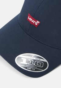 Gorra de béisbol azul marino hecha de una mezcla de algodón, con un logo de Levi's bordado en rojo y una etiqueta Flexfit Tech en la visera.