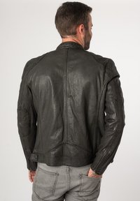 Schwarze Leder-Motorradjacke mit strukturierter Oberfläche, kantigem Design, Reißverschlusstaschen und genähten Details auf Schultern und Rücken.