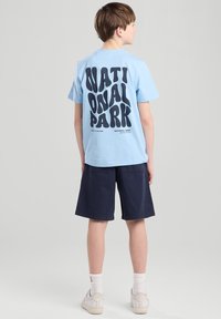 Light blue cotton t-shirt with bold black text "NATIONAL PARK" on the back, paired with navy shorts and white sneakers.
