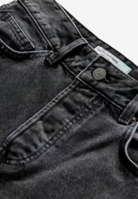 Vaqueros de mezclilla negra con un ajuste relajado, con cierre de botones, trabillas para cinturón y un sutil desgaste. Etiqueta visible cerca de la pretina.