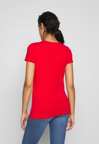 Rød bomulds T-shirt med korte ærmer, tætsiddende form, rund halsudskæring og en glat struktur. Båret sammen med blå denim jeans.