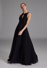Schwarzes ärmelloses Kleid mit einem taillierten, bestickten Oberteil, einem Ausschnitt mit Schlüsselöffnung und einem fließenden Rock aus leichtem Material.