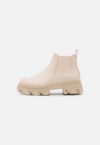 Beżowe botki Chelsea wykonane ze skóry, z elastycznymi panelami bocznymi i grubą gumową podeszwą z głębokim bieżnikiem dla lepszej przyczepności i stabilności.