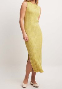 Robe en maille côtelée jaune ondulée avec une fente latérale et un design sans manches, associée à des ballerines de couleur claire ornées d'un nœud.