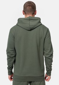 Zelená mikina s kapucňou vyrobená z mäkkej tkaniny, vybavená klokaním vreckom, ribovanými manžetami a lemom, a kapucňou s nastavovacou šnúrkou.