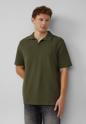 Donkergroene polo met kraag en korte mouwen, gemaakt van een gestructureerde stof. Gepaard met donkergrijze jeans voor een casual look.