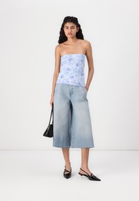 Brezrokavni svetlo modri top z cvetličnim potiskom, v kombinaciji z širokimi svetlimi denim culotami. Dodatki vključujejo črno torbico in čevlje s koničastim sprednjim delom.
