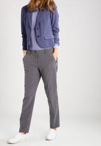 Granatowa marynarka z dwoma guzikami, noszona na jasnoniebieskiej koszuli w wzory, w zestawieniu ze spodniami w kolorze szarym, dopasowanymi i białymi butami wsuwanymi.