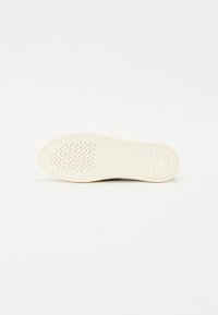 Biela podrážka obuvi s textúrovaným povrchom, ktorá obsahuje malé perforácie a vzor so zúbkami. Pevný, flexibilný dizajn pre pohodlie a trakciu.