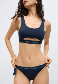 Σετ μπικίνι σε ναυτικό μπλε χρώμα με τοπ με λαιμόκοψη scoop και λεπτομέρεια με ανοίγμα, καθώς και αντίστοιχα χαμηλόμεσα κάτω μέρη, και τα δύο με το λογότυπο "TOMMY HILFIGER".
