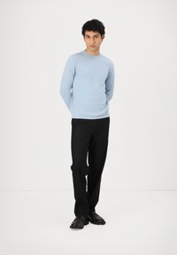 Helles blaues Langarm-Sweatshirt aus weichem Material, kombiniert mit schwarzen Hosen. Das Outfit beinhaltet schwarze Schuhe und steht vor einem weißen Hintergrund.