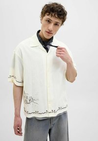 Chemise à manches courtes, jaune clair avec un motif texturé subtil, présentant un dessin en ligne marron à l'ourlet et un design de col.
