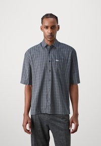 Short-sleeved plaid shirt in navy and grey, featuring a button-down front, a small pocket, and a label on the chest. Smooth fabric texture.