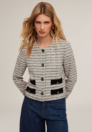 Black and white patterned jacket with a round neck, button front, and black velvet accents on pockets. Featured in a structured fit.