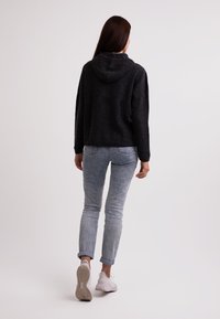 Felpa nera con cappuccio e vestibilità comoda; indossata con jeans azzurri chiari e sbiaditi; scarpe da ginnastica bianche. Texture morbida, stile casual.