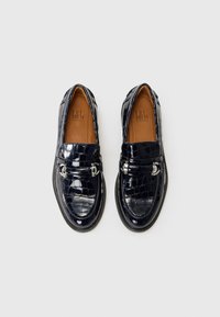 Tumedan patentnahast loafers krokodillimustriga, hõbedane pandla detail ja must kummitald. Sile viimistlus ja ümar nina disain.