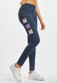 Navy legging in een rekbaar materiaal, met drie bedrukte ontwerpen van palmboom tegen vierkante achtergronden in lichte kleuren.